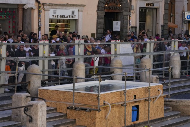 Tourists toss coins over a makeshift pool as Rome’s Trevi Fountain undergoes maintenance