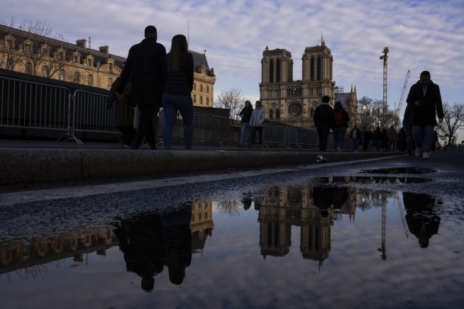 An archbishop's knock formally restores Notre Dame to life as winds howl and heads of state look on